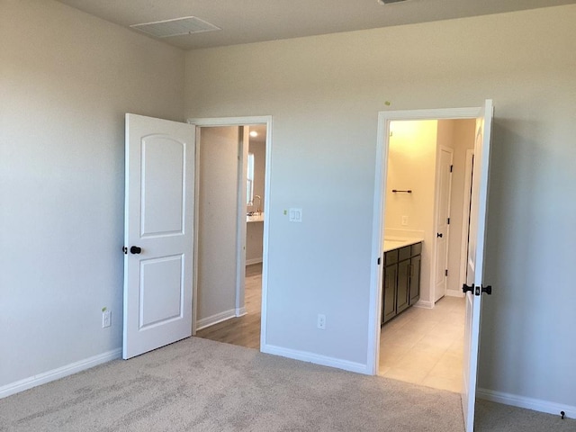 unfurnished bedroom featuring baseboards, visible vents, ensuite bathroom, and light carpet