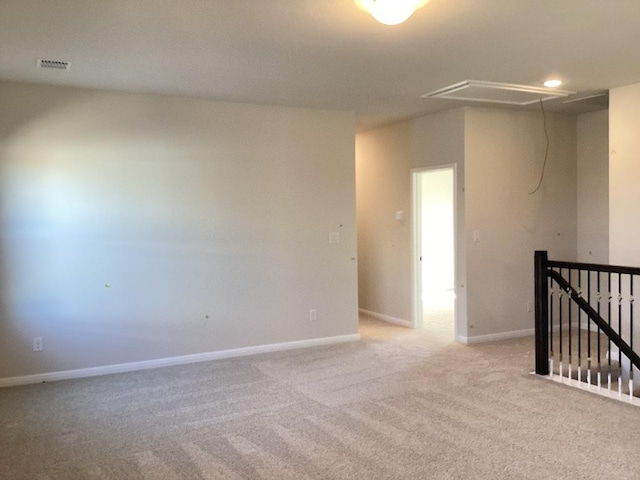 carpeted spare room featuring visible vents, attic access, and baseboards