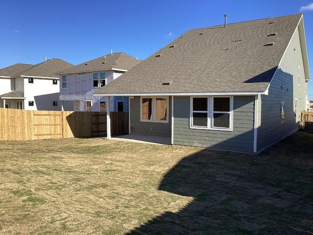 rear view of house with a yard, a patio area, a shingled roof, and fence