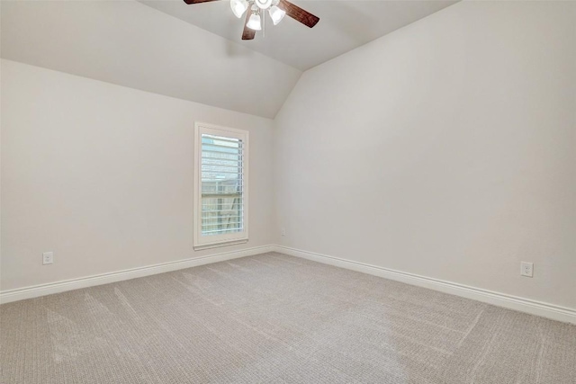 spare room featuring vaulted ceiling, light colored carpet, baseboards, and ceiling fan