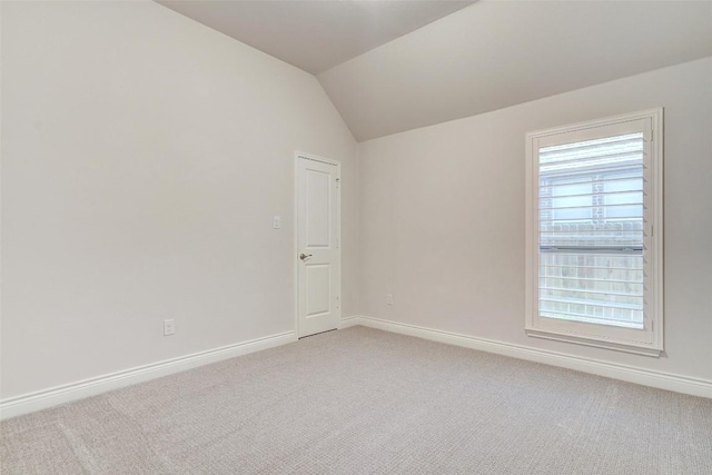 empty room featuring baseboards, light carpet, and vaulted ceiling