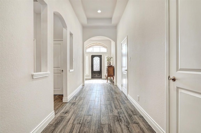 entrance foyer with baseboards, arched walkways, a raised ceiling, and dark wood-style floors