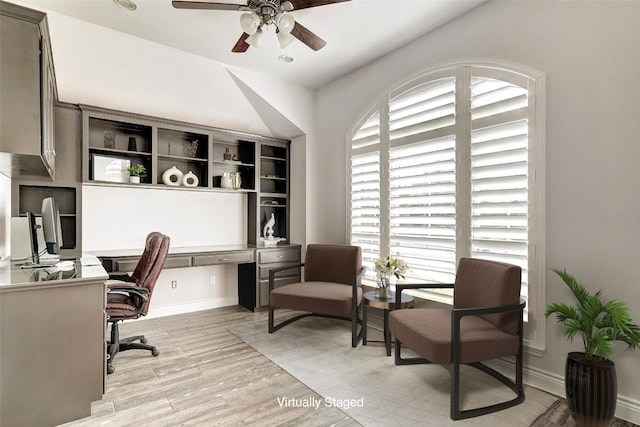 office space featuring baseboards, built in desk, light wood-style flooring, and a ceiling fan