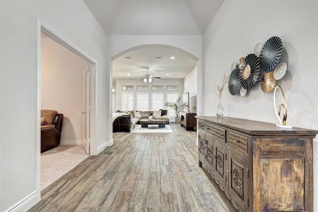 hallway with baseboards, vaulted ceiling, recessed lighting, light wood-style floors, and arched walkways