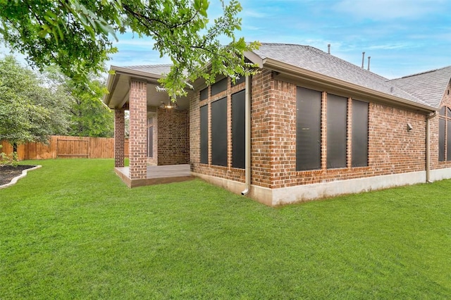 view of property exterior featuring brick siding, a lawn, a shingled roof, and fence