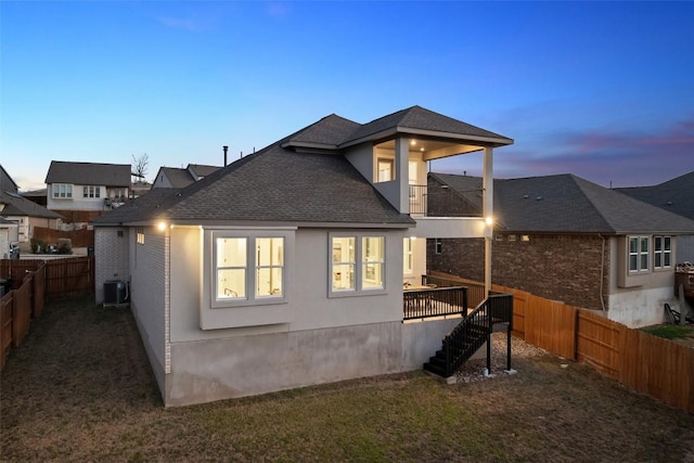 back of property at dusk featuring a shingled roof, central air condition unit, stairway, stucco siding, and a fenced backyard