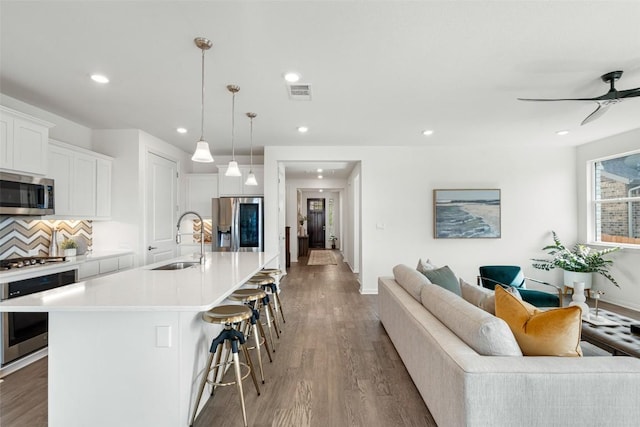 kitchen featuring a breakfast bar area, visible vents, stainless steel appliances, a sink, and open floor plan