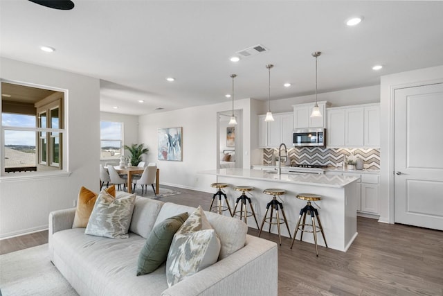 living room with recessed lighting, visible vents, baseboards, and wood finished floors