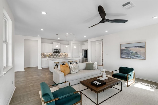 living room featuring a ceiling fan, baseboards, visible vents, recessed lighting, and light wood-type flooring