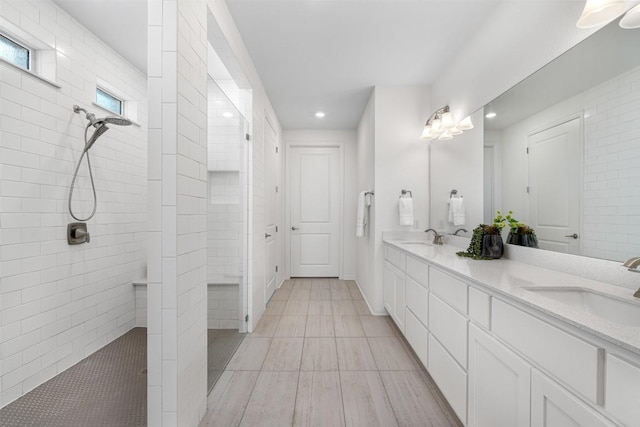 full bathroom featuring double vanity, tiled shower, and a sink