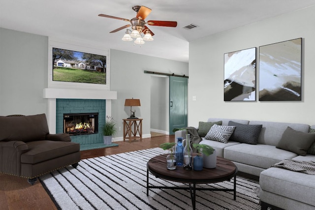 living room featuring a ceiling fan, a barn door, wood finished floors, and visible vents