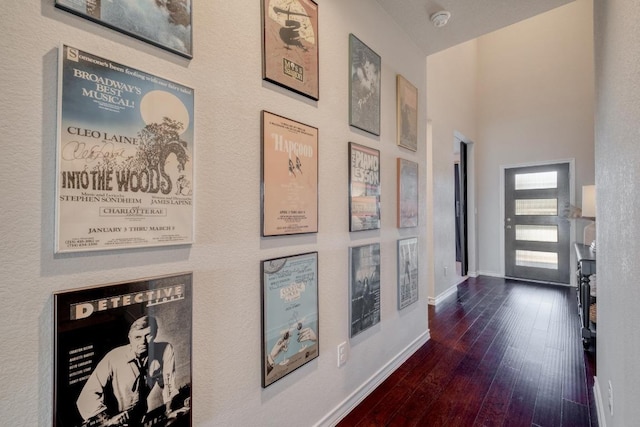 corridor featuring dark wood finished floors, baseboards, and a towering ceiling