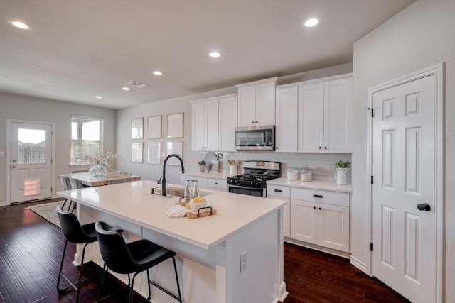 kitchen featuring visible vents, a sink, decorative backsplash, stainless steel appliances, and a kitchen island with sink