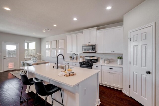 6717 Catania Loop, Round Rock, TX 78665 - kitchen with stainless steel appliances, a kitchen island with sink, dark wood-type flooring, white cabinets, and backsplash
