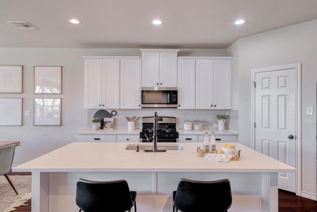 kitchen featuring range with gas stovetop, visible vents, an island with sink, stainless steel microwave, and tasteful backsplash