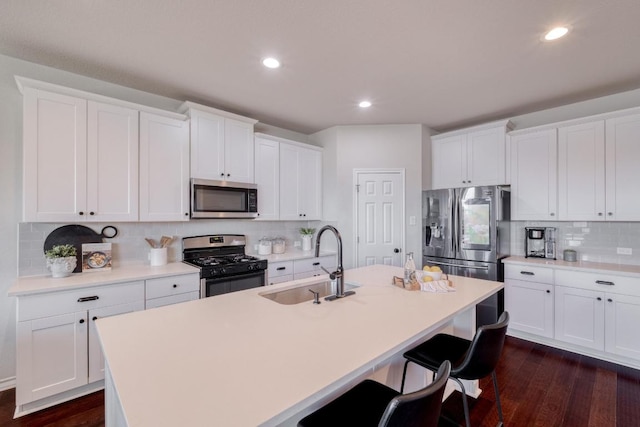 kitchen featuring a kitchen bar, a kitchen island with sink, a sink, white cabinetry, and stainless steel appliances