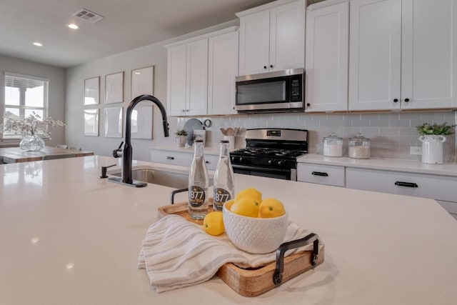 kitchen with visible vents, stainless steel appliances, decorative backsplash, light countertops, and white cabinets