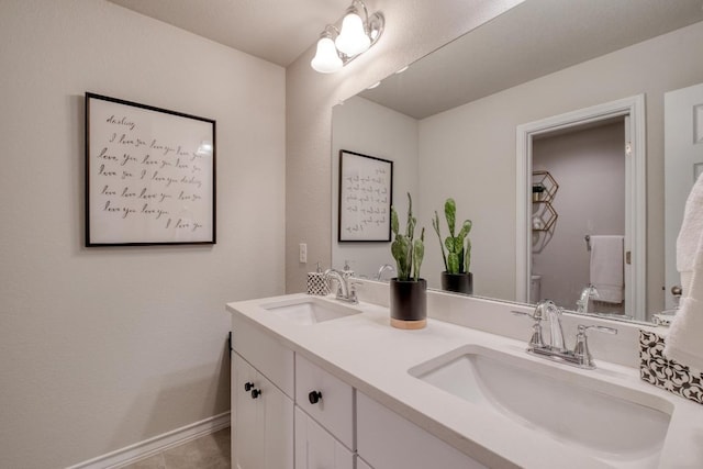 bathroom featuring double vanity, toilet, baseboards, and a sink