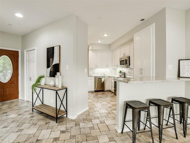 kitchen with light countertops, white cabinets, appliances with stainless steel finishes, a kitchen breakfast bar, and tasteful backsplash