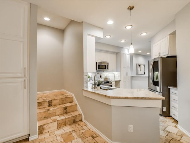 kitchen with stone tile floors, appliances with stainless steel finishes, white cabinets, decorative backsplash, and hanging light fixtures