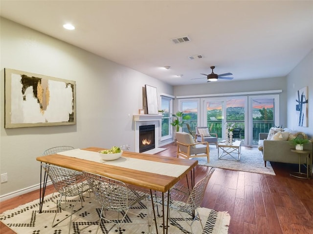 dining area featuring a ceiling fan, wood finished floors, visible vents, and a lit fireplace