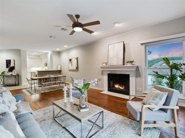 living area with visible vents, a fireplace with flush hearth, a ceiling fan, and wood finished floors