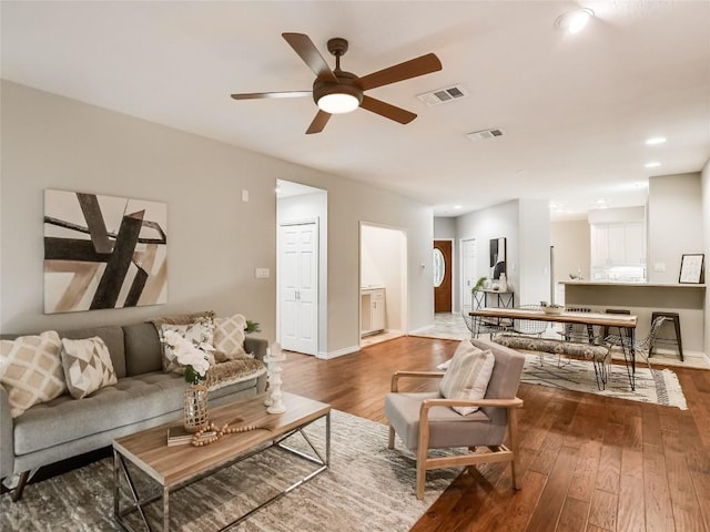 living area featuring hardwood / wood-style flooring, a ceiling fan, visible vents, and baseboards