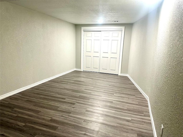 unfurnished bedroom with baseboards, a textured ceiling, dark wood finished floors, and a textured wall