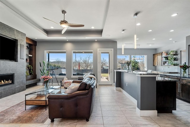 living room with recessed lighting, a tray ceiling, a ceiling fan, and a premium fireplace