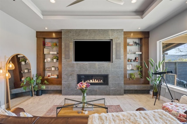 living room featuring built in shelves, a tile fireplace, and a raised ceiling