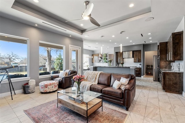 living room with a tray ceiling, recessed lighting, a ceiling fan, and baseboards