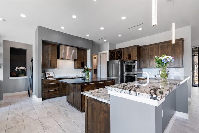 kitchen with a kitchen island, appliances with stainless steel finishes, dark brown cabinetry, and wall chimney range hood