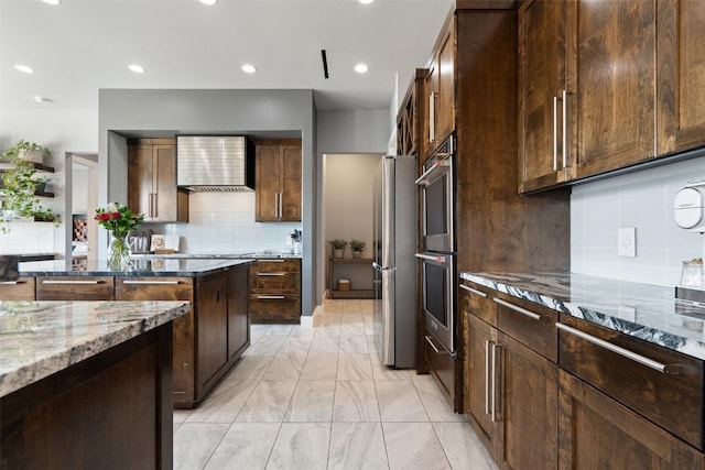 kitchen with marble finish floor, dark stone countertops, tasteful backsplash, stainless steel appliances, and wall chimney exhaust hood