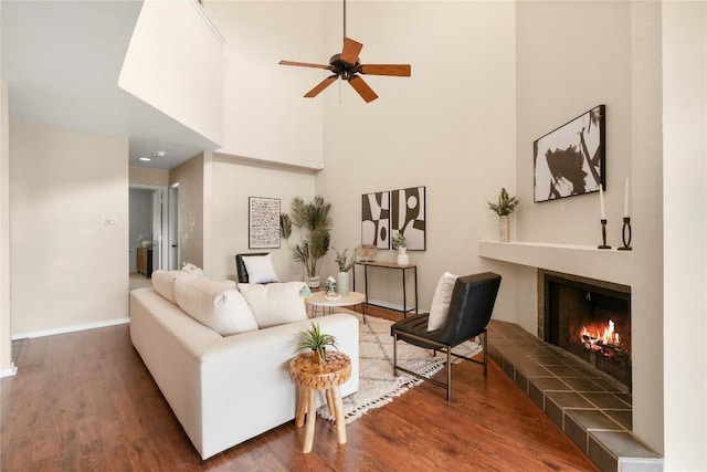 living room with baseboards, a ceiling fan, wood finished floors, and a tiled fireplace