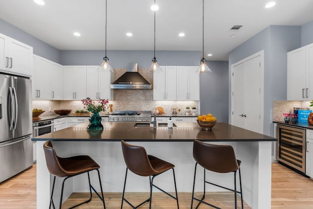 kitchen with beverage cooler, a sink, dark countertops, stainless steel appliances, and wall chimney exhaust hood