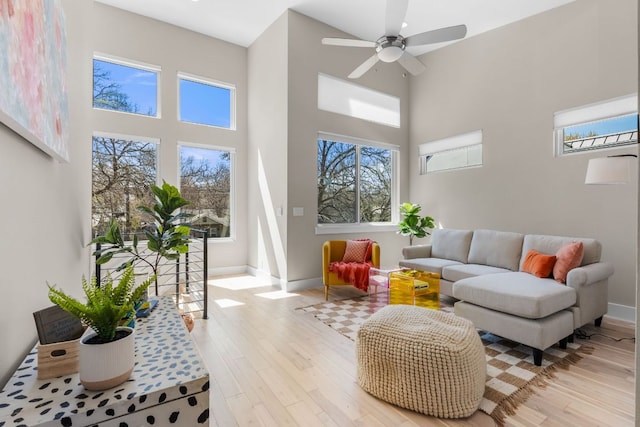 living area with a towering ceiling, a ceiling fan, baseboards, and wood finished floors