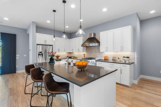 kitchen featuring dark countertops, tasteful backsplash, light wood-type flooring, appliances with stainless steel finishes, and wall chimney exhaust hood