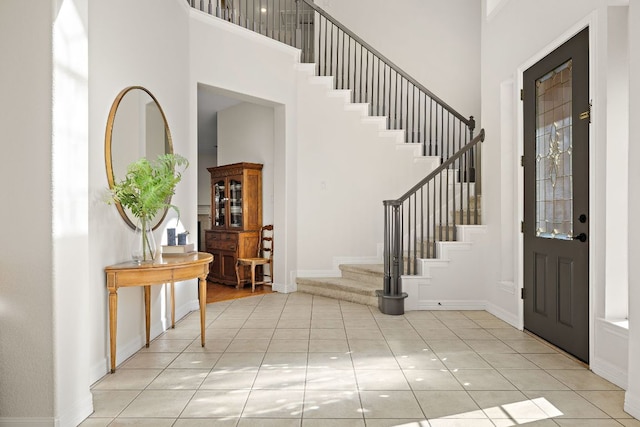 entryway with light tile patterned floors, baseboards, stairs, and a towering ceiling