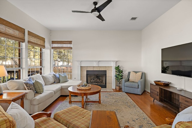 living room featuring visible vents, wood finished floors, a ceiling fan, and a tiled fireplace