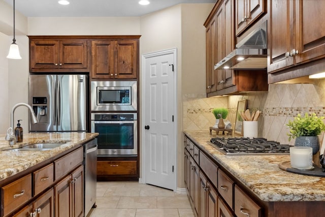 kitchen featuring under cabinet range hood, light stone counters, decorative backsplash, stainless steel appliances, and a sink