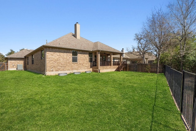 rear view of house with a yard, central air condition unit, brick siding, and a fenced backyard