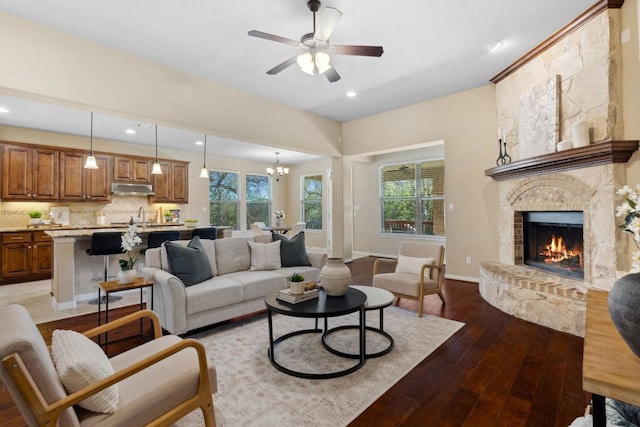 living room featuring a wealth of natural light, wood-type flooring, a fireplace, and ceiling fan with notable chandelier