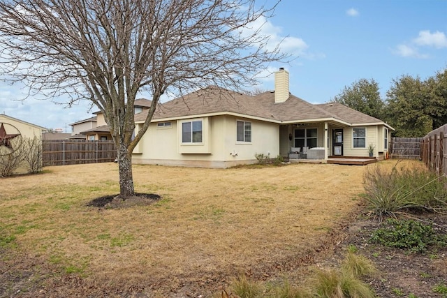 rear view of property with a deck, a lawn, a chimney, and a fenced backyard