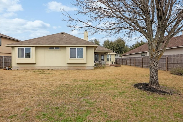 rear view of property featuring roof with shingles, a lawn, a fenced backyard, and a chimney