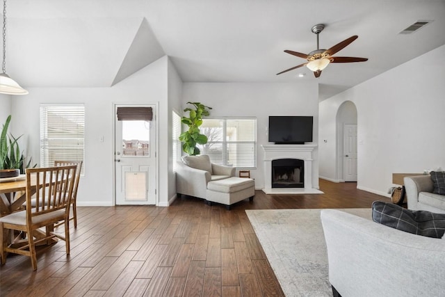 living room with visible vents, a fireplace with raised hearth, arched walkways, ceiling fan, and dark wood-type flooring