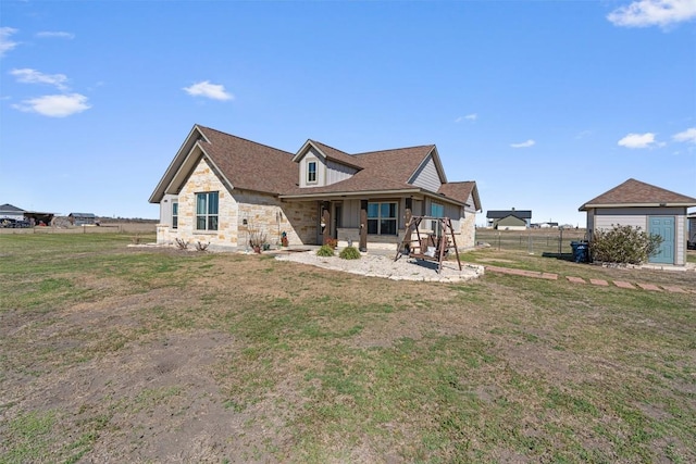 back of house with a shingled roof, fence, a lawn, an outbuilding, and stone siding