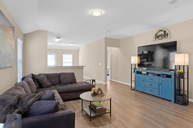 living area featuring light wood finished floors, visible vents, lofted ceiling, and baseboards