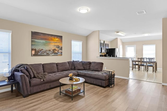 living room featuring light wood finished floors, visible vents, baseboards, and lofted ceiling