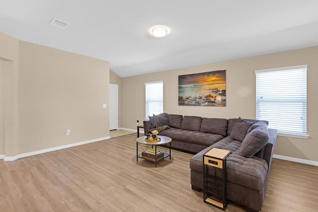 living area featuring visible vents, baseboards, light wood-style flooring, and vaulted ceiling