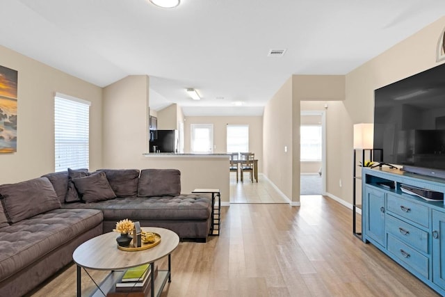 living room featuring light wood finished floors, visible vents, baseboards, and vaulted ceiling